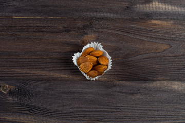 a portion of almonds in a paper muffin on a dark wood background