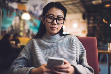 Content Asian woman browsing smartphone in cafe