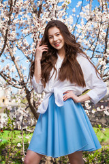 Pretty teen girl are posing in garden near blossom cherry tree with white flowers