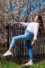 Portrait of a young stylish girl in in blue jeans against the background of blooming cherry