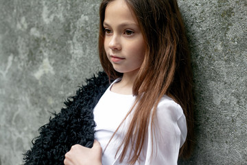 Young preteen girl dressed black and white clothes posing with hands against grey wall  in the street of the city