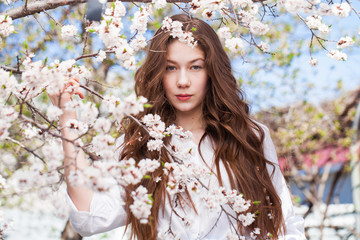 Pretty teen girl are posing in garden near blossom cherry tree with white flowers