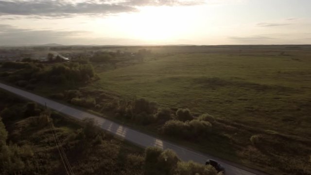 Flying over the concrete road with a moving vehicle. Stock footage. Aerial view of countryside landscape with green field, forest and the road with a driving car on a sunny summer day.