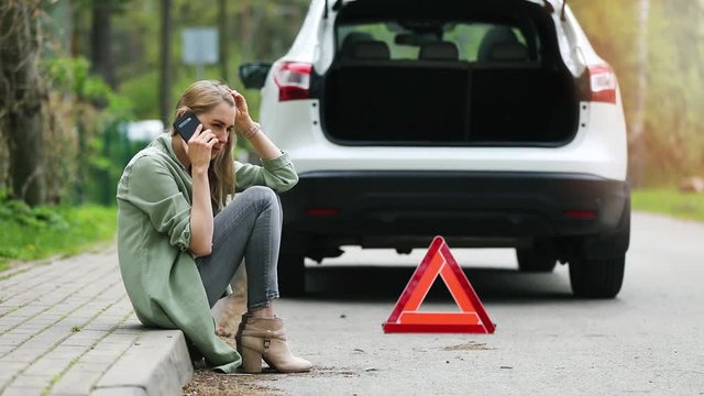woman is sitting on the side of the road and calling for help because broken car