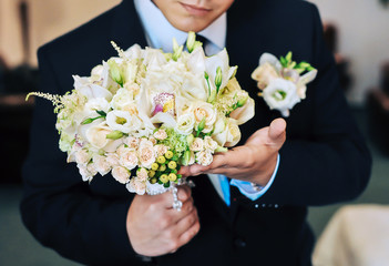Obraz na płótnie Canvas The groom in a dark suit holds a wedding bouquet. Close-up