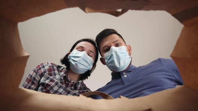 Happy couple opening cardboard box looking inside, delivery on coronavirus quarantine home isolation, portraits with medical masks and protection gloves, e-commerce, food courier.