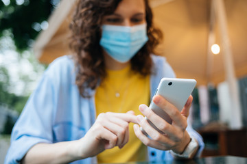 Fototapeta premium Young woman in medical face mask uses her mobile phone