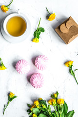 woman desk with marsh-mallow and flowers on white marble background top view
