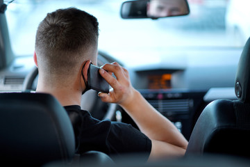 a guy, a young man in a black t-shirt with a black mask sitting behind the wheel, talking on the phone, during the day, rear view