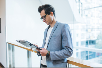 Well dressed employee standing with clipboard in office