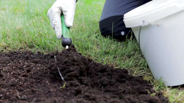 slow motion, close up, gardener is putting fresh soil with a hand shovel on new seeds