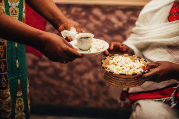 African women's hands holding a cup of coffee and straw bowl with popcorn, a traditional way of...