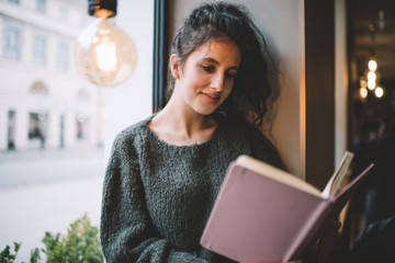 Cheerful lady reading book sitting near window