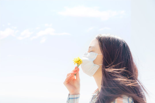Young Woman In Protective Mask Smelling Yellow Flowers Outdoor.