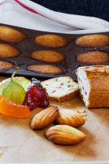 On a wooden table, a composition of home-made pastries including confiscated fruits, a cake with sliced fruits as well as madeleines alone and some not yet unmoulded.