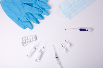 Tablets, gloves, vaccine, syringe-thermometer on a white background. The concept of protection from viruses. Flat styling, top view, copy space