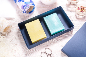 Set of blue and yellow  handmade soap in carton box on wooden background, top view, mockup