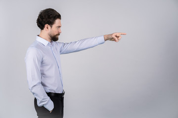 A man with a beard in a white shirt standing on white background and pointing in the direction