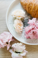 Fototapeta na wymiar Croissant on a white plate with flowers. Nice breakfast. Concept of coffee shop and flower shop.