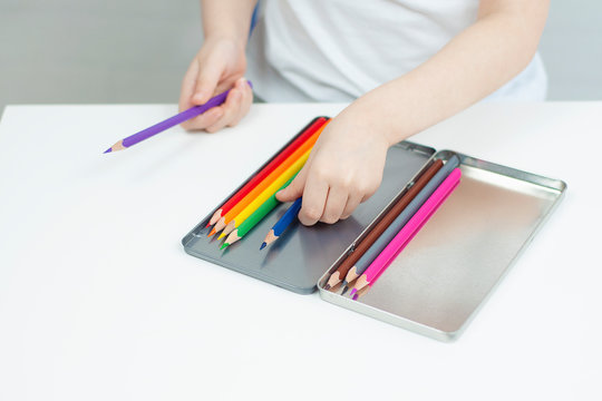 A child puts color pencils in a box. Children's development. Selective focus