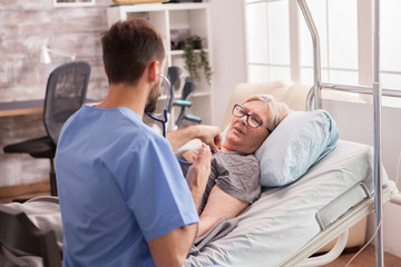 Obraz premium Back view of male doctor using stethoscope to check woman heart in nursing home.