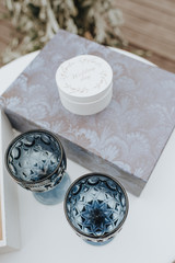 Two blue glasses of wine stand on a table. Nearby is a white round box for engagement rings.