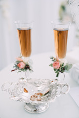Two glasses of champagne stand on a table stand on a table. The legs of the glasses are decorated with bouquets of roses and green leaves.