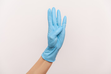 Obraz premium Profile side view closeup of human hand in blue surgical gloves showing number four 4 with hand. indoor, studio shot, isolated on gray background.