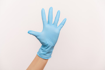 Profile side view closeup of human hand in blue surgical gloves showing number five with hand or...