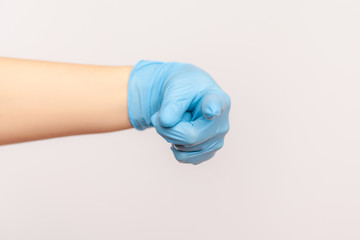 Fototapeta premium Profile side view closeup of human hand in blue surgical gloves showing or pointing at camera. indoor, studio shot, isolated on gray background.