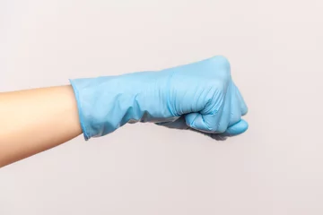 Foto op Plexiglas Profile side view closeup of human hand in blue surgical gloves showing boxing fists with hand. attack or defence against problems. indoor, studio shot, isolated on gray background. © khosrork