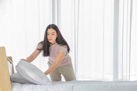 Asian lady making bed in her morning routine after wake up for tidying up the bedroom in soft light with copy space