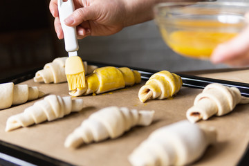 Baking croissants at home and covering the dough with egg yolk using pastry brush