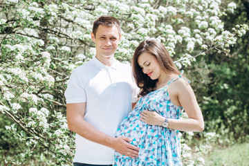 Fototapeta premium Young parents walk in the park on a warm spring day. Pregnant young woman in nature. Happy future parents. Waiting for a miracle.