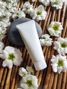 Mock up of white plastic bottle tube with white flowers and stone on a bamboo background. Natural organic cosmetics concept. Lifestyle, flat lay