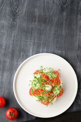 Caprese is a traditional Italian vegetable salad with mozzarella cheese, cherry tomatoes and arugula microgreens. Top view with copy space. Dark wooden rustic background.