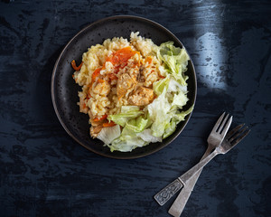 Breakfast with rice and meat. Fresh shredded iceberg lettuce. Serving on a black plate on a dark background.