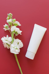 blank white squeeze bottle plastic tube on a burgundy background with a white flower.  View from above, space for a text. 