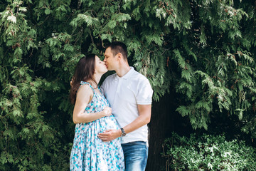 Young parents walk in the park on a warm spring day. Pregnant young woman in nature. Happy future parents. Waiting for a miracle.