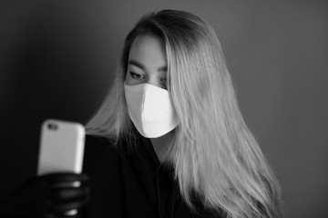 Portrait of a young woman in a white medical mask and black gloves with long blond hair is looking...