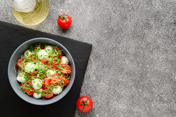 Italian food. Delicious caprese salad with mozzarella cheese, cherry tomatoes and arugula microgreens. Top view with copy space. Gray stone background.