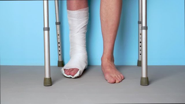 A man with a broken leg in a cast is slowly walking on a walker on a blue background. Slow motion.