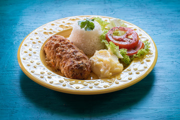 Food plate. Lunch. Breaded, rice, mashed potatoes and salad. Blue background.