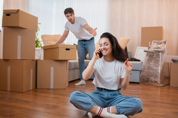 Moving and relationship concept. He is not satisfied. The husband unpacks the boxes. And the wife meanwhile does nothing. She prefers to talk to her friends. The husband is not satisfied