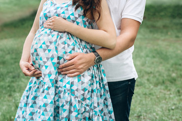 Young parents walk in the park on a warm spring day. Pregnant young woman in nature. Happy future parents. Waiting for a miracle.