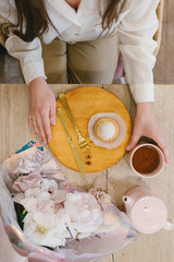 Shu cake on a wooden plate, flowers, a cup of tea and female hands in the frame. Concept of cafe and pastry shop. Stylish breakfast.