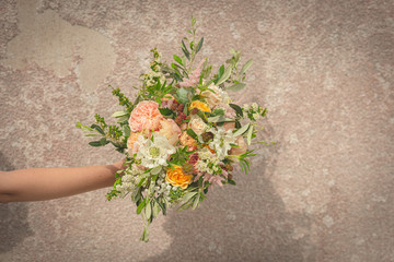 Hand holding a beautiful wedding bouquet in front of a rustic wall..