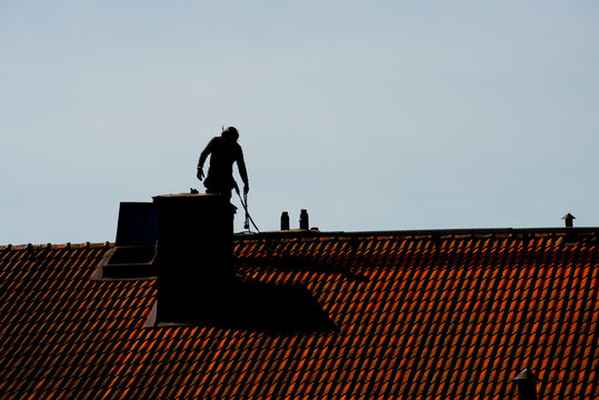 Silhouette of a chimney sweeper on top of a roof..