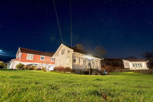 Long exposure photo of a white wooden house and garden at night.