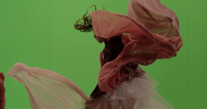 Close up portrait of beautiful fashion model dancer posing against green screen with billowing fabric surrounding her